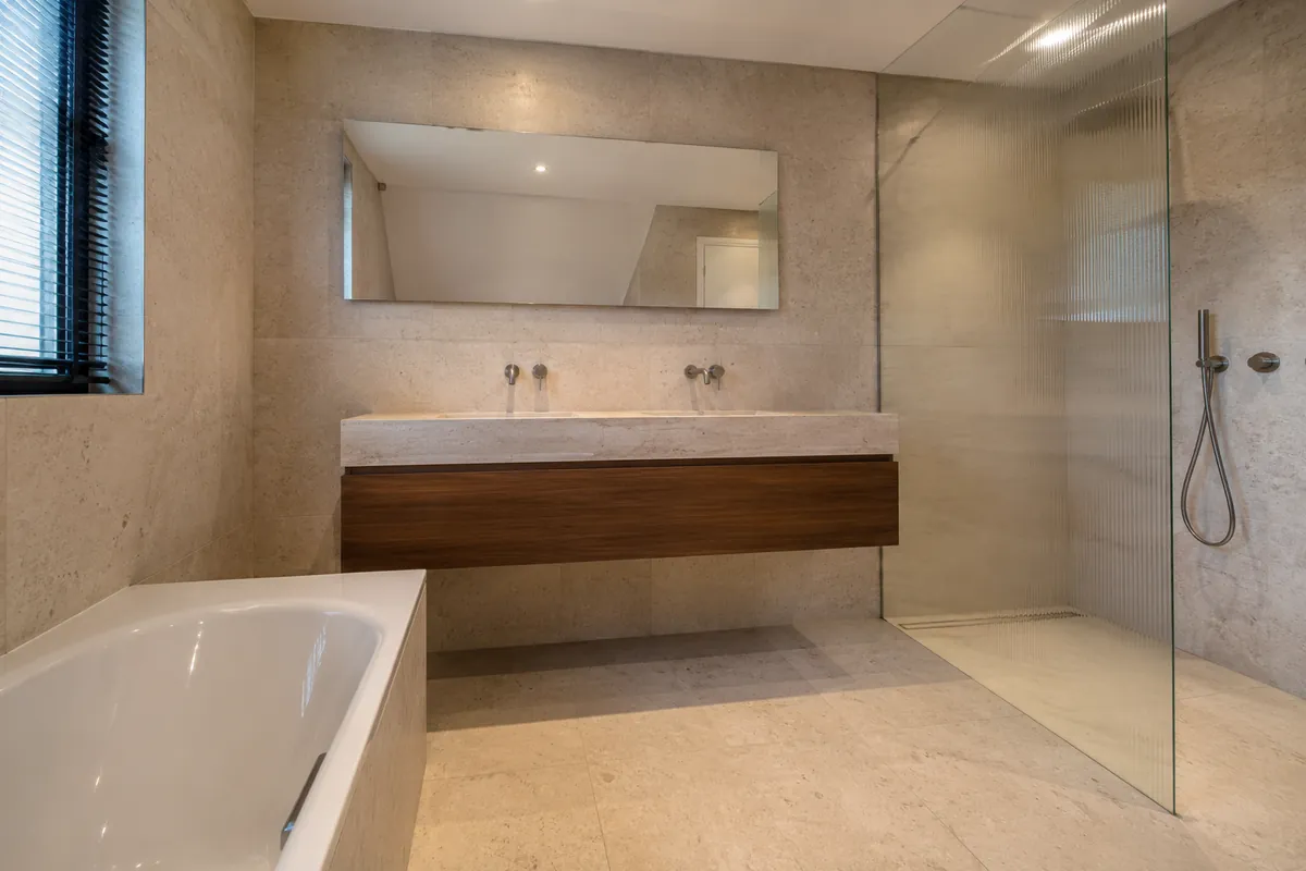 Badkamer met travertin tegels en notenhouten meubel, Bussum